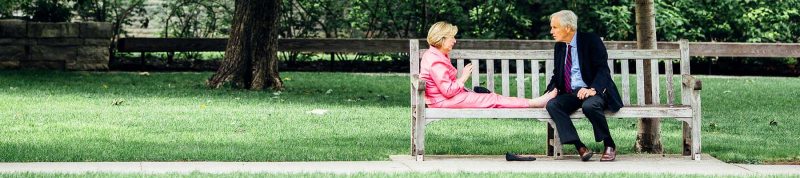 Image depicts two people sitting on a bench one with their feet up and they are looking at each other