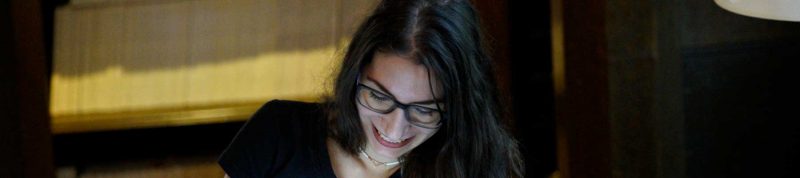 Image depicts a student in a library smiling at the computer