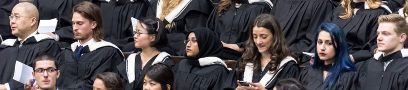 Image depicts student dressed in convocation robes sitting in convocation hall