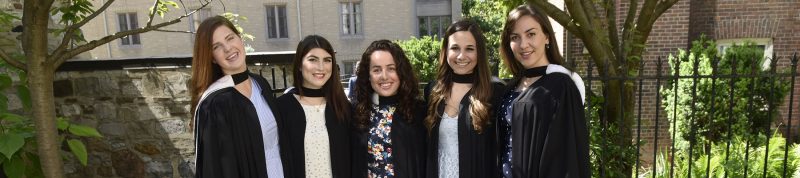 Image depicts 5 students standing posing for a photo in convocation gowns