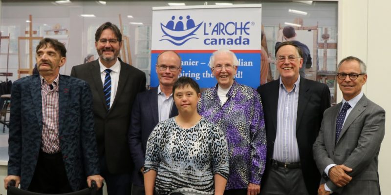 Image depicts a group of people standing in front of a banner for L'arche Canada