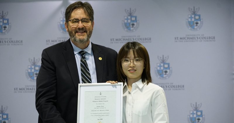 Image depicts Dr. David Sylvester with USMC graduate Jinman Zhao getting graduation award