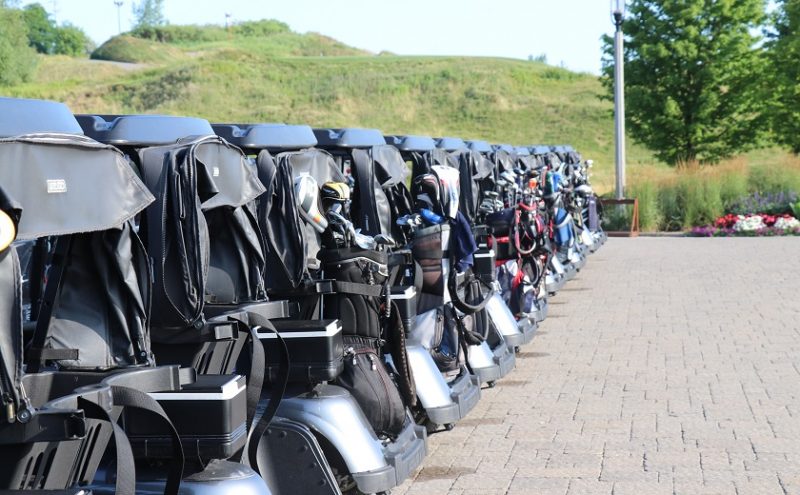 Image depicts a line of golf carts with golf bags on them