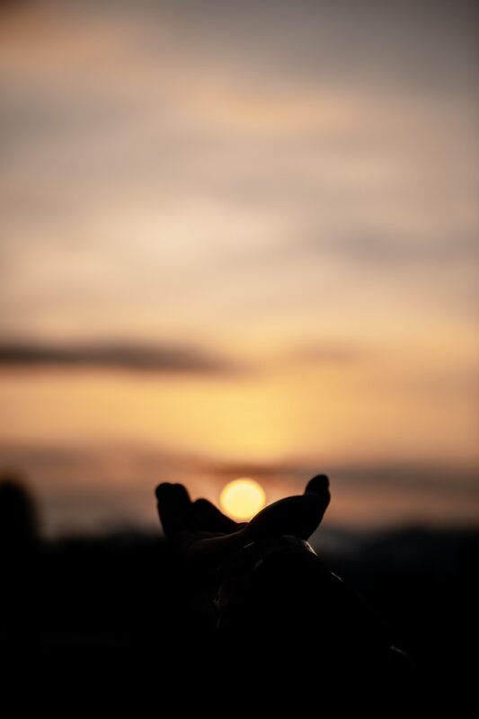 Image shows a person cupping their hands against the sky, creating the illusion that they are holding the setting sun