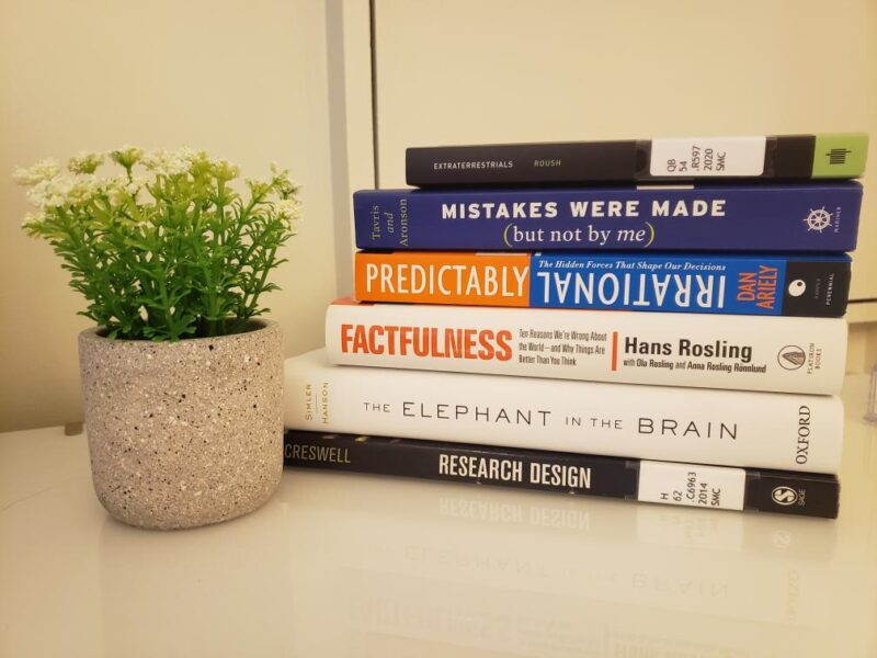 Photograph of Risa's books: Extraterrestrials; Mistakes Were Made (But Not By Me); Predictably Irrational; Factfulness; The Elephant in the Brain; Research Design