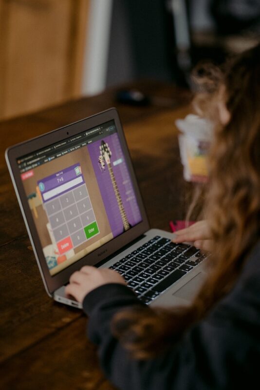 Photograph of girl looking at a math problem on a laptop