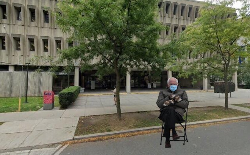 The Kelly Library, with Bernie Sanders portrayed in hat and gloves on a folding chair in the street in front of the building