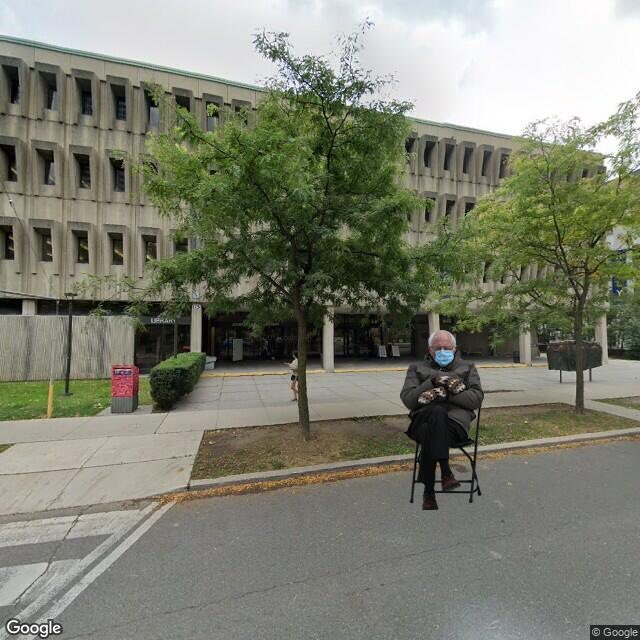 The Kelly Library, with Bernie Sanders portrayed in hat and gloves on a folding chair in the street in front of the building 