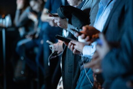 A row of men in suits holding smartphones at an indoor event 