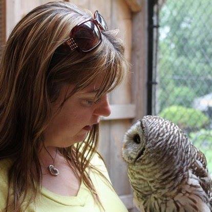 Photograph of Angela MacAloney-Mueller looking down at a brown and grey owl, which is only inches away from her and looking back up at her.