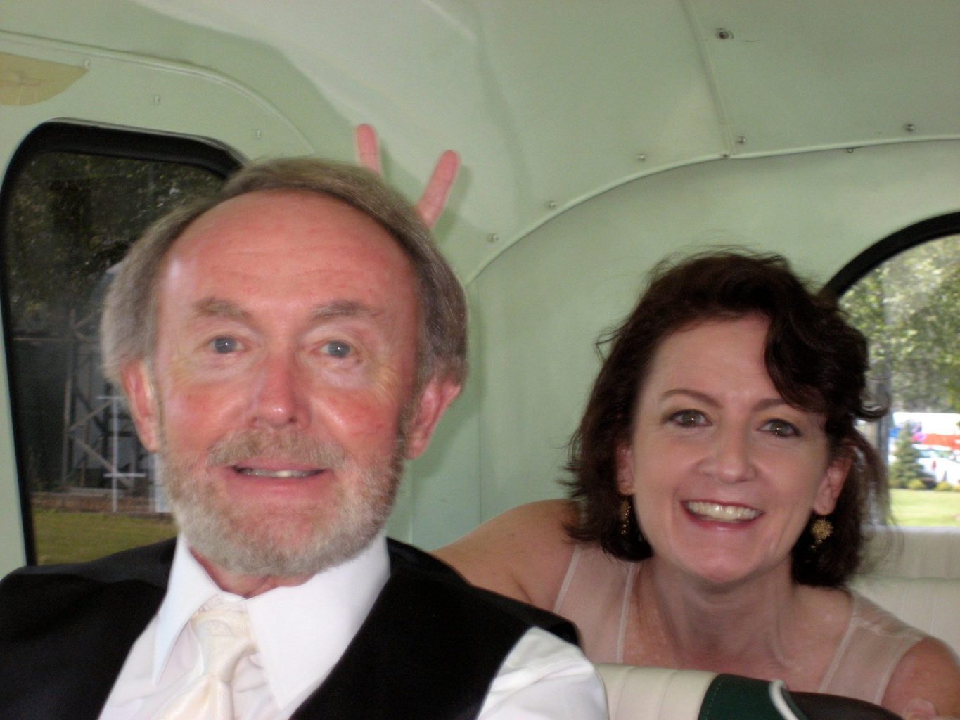 Photograph of Laurie Morris and her father sitting in formal wear in the back of a vehicle. Laurie is doing "bunny ears" behind her dad's head.