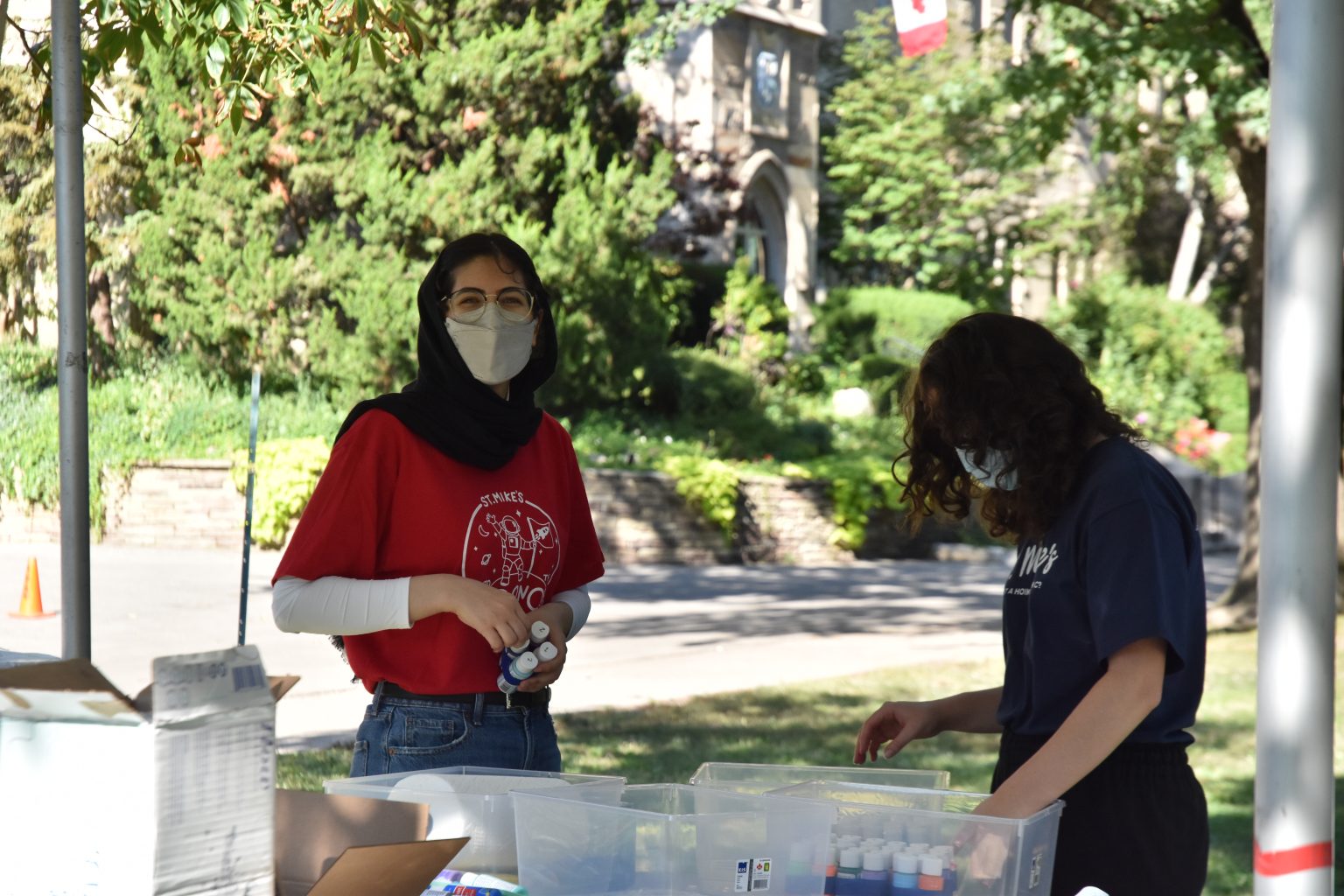 Photograph of two St. Mike's orientation leaders (wearing masks) organizing art supplies under a tent on campus