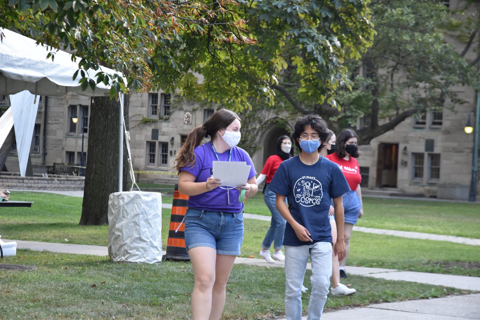 Photograph of two St. Mike's orientation leaders (wearing masks) walking toward the camera with the campus quad in the background