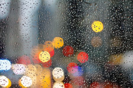 Photograph of rain droplets on a window with city lights out of focus in the background.