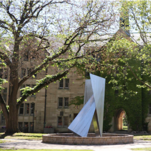 A metallic abstract sculpture installation in the middle of a fountain on the St. Mike's quad on a sunny day