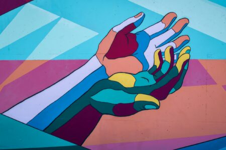 Photograph of a wall mural of two hands outstretched and supporting one another, in a bright mosaic of colours.