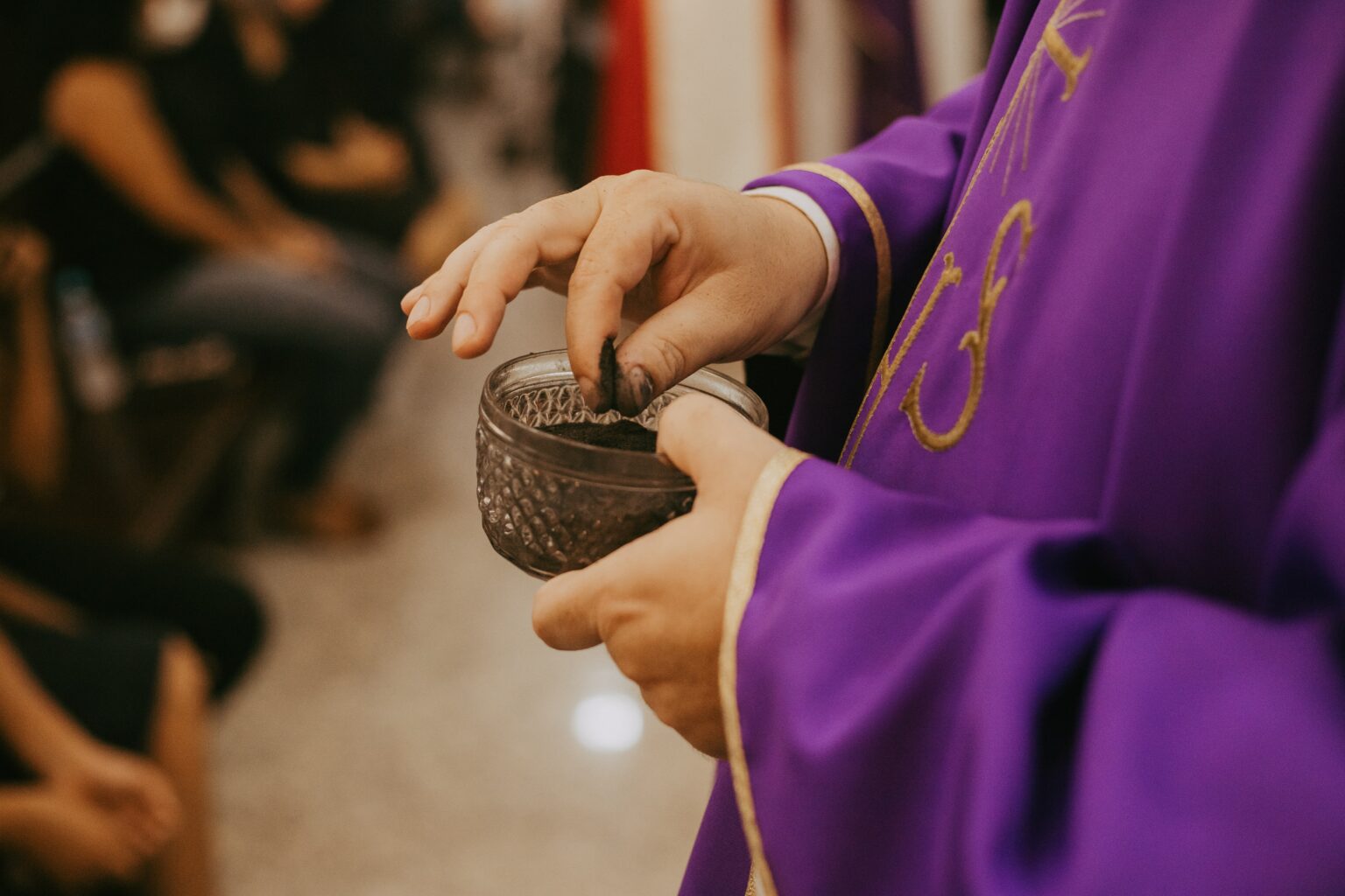 Detail of a priest in vestments for Lent pinching ash out of a glass dish 