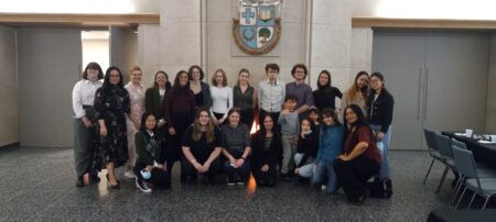 A group of students stand in front of a hearth with the St. Michael's logo on the wall above them